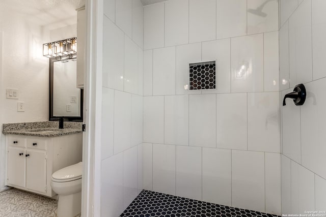 bathroom with a tile shower, vanity, and toilet