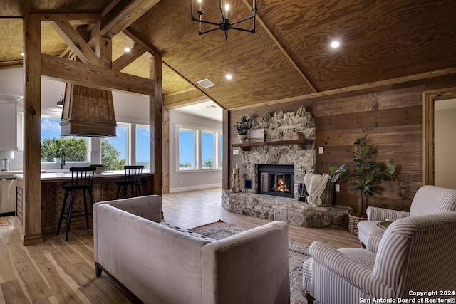 living room with wooden ceiling, lofted ceiling with beams, a stone fireplace, wooden walls, and light hardwood / wood-style floors