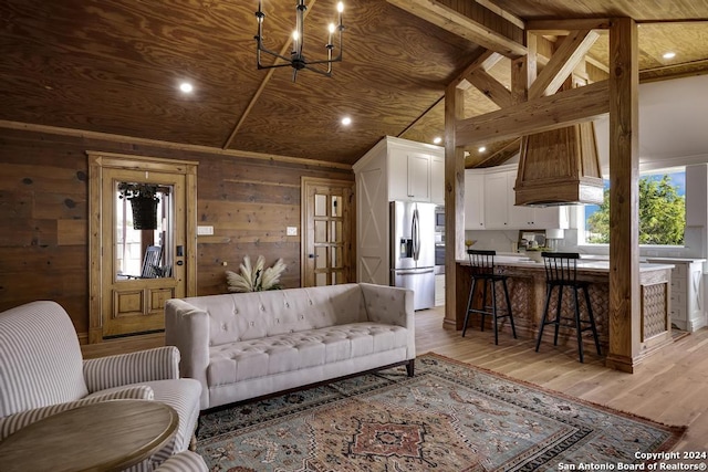 living room with wood walls, an inviting chandelier, vaulted ceiling with beams, light wood-type flooring, and wood ceiling