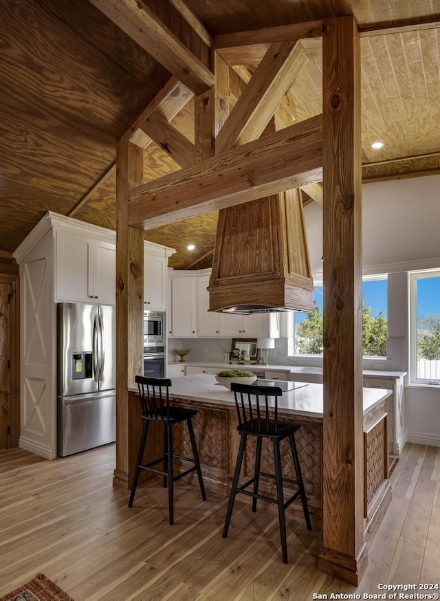 kitchen featuring appliances with stainless steel finishes, custom exhaust hood, a breakfast bar, light hardwood / wood-style flooring, and white cabinets