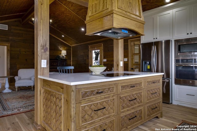 kitchen with white cabinets, wood walls, light hardwood / wood-style floors, and stainless steel appliances