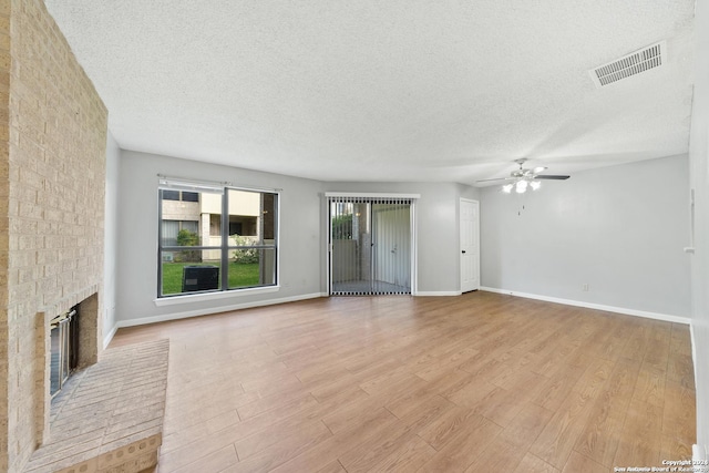 unfurnished living room featuring ceiling fan, a fireplace, light hardwood / wood-style floors, and a textured ceiling