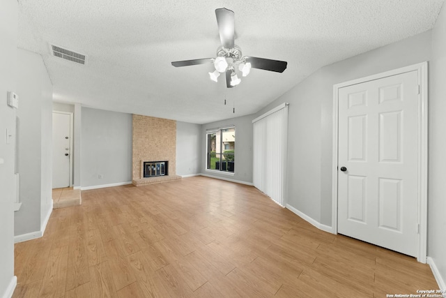 unfurnished living room featuring a fireplace, a textured ceiling, light hardwood / wood-style flooring, and ceiling fan