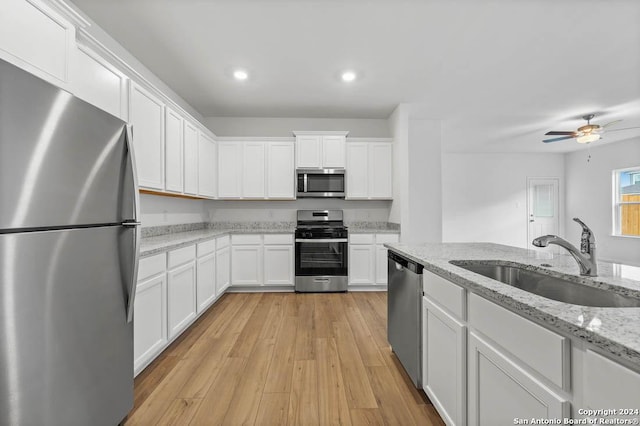 kitchen with light stone countertops, appliances with stainless steel finishes, sink, light hardwood / wood-style flooring, and white cabinetry