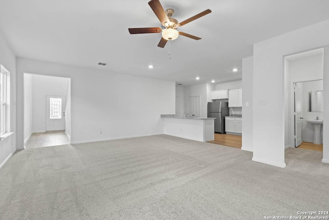 unfurnished living room featuring ceiling fan, sink, and light colored carpet