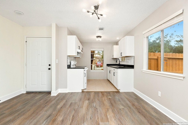 kitchen with sink, light hardwood / wood-style flooring, backsplash, a textured ceiling, and white cabinets