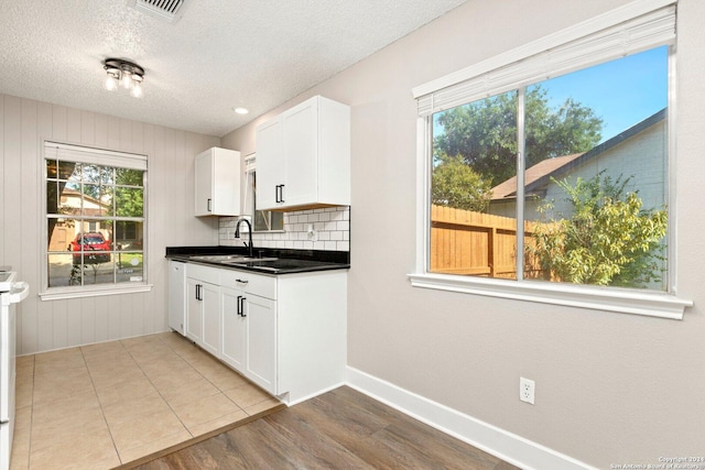 kitchen featuring tasteful backsplash, a textured ceiling, sink, white cabinets, and light hardwood / wood-style floors