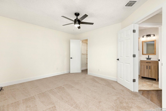 unfurnished bedroom featuring ceiling fan, sink, ensuite bathroom, light colored carpet, and a textured ceiling