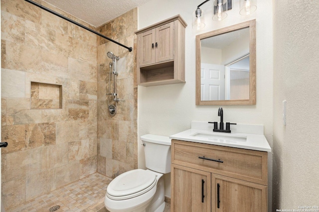 bathroom featuring a tile shower, vanity, a textured ceiling, and toilet