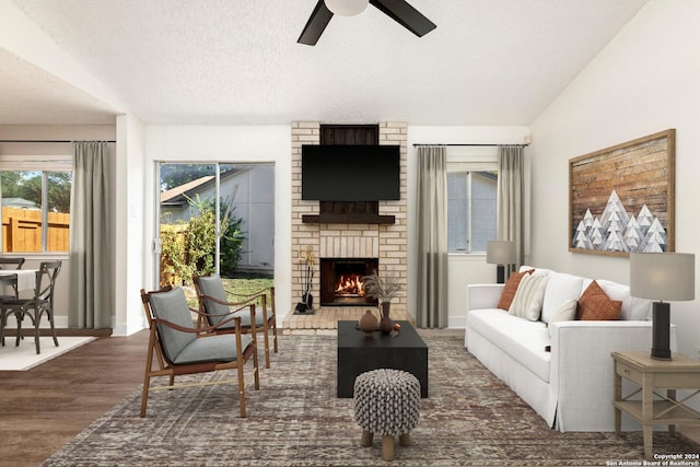 living room featuring dark hardwood / wood-style flooring, a brick fireplace, a textured ceiling, vaulted ceiling, and ceiling fan