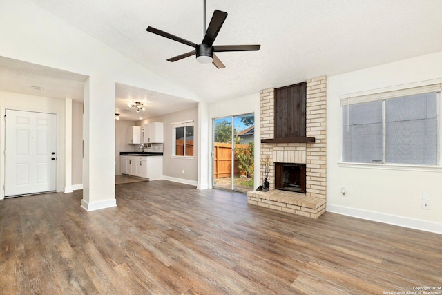 unfurnished living room with hardwood / wood-style floors, vaulted ceiling, ceiling fan, a fireplace, and a textured ceiling