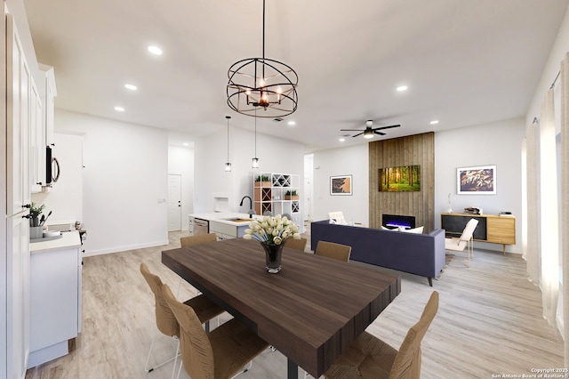 dining room featuring light wood-type flooring, a large fireplace, ceiling fan with notable chandelier, and sink