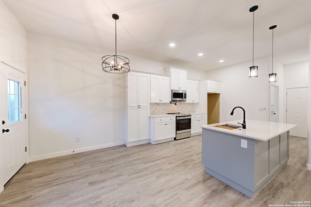 kitchen featuring a center island with sink, white cabinets, sink, appliances with stainless steel finishes, and decorative light fixtures