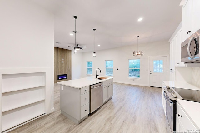 kitchen featuring appliances with stainless steel finishes, ceiling fan, a kitchen island with sink, white cabinets, and hanging light fixtures