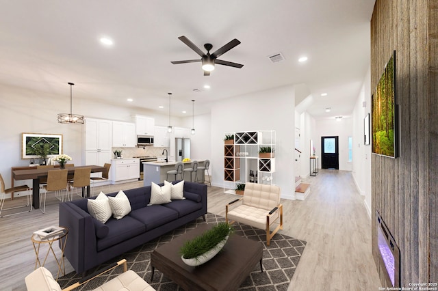 living room with ceiling fan with notable chandelier, light hardwood / wood-style flooring, and sink