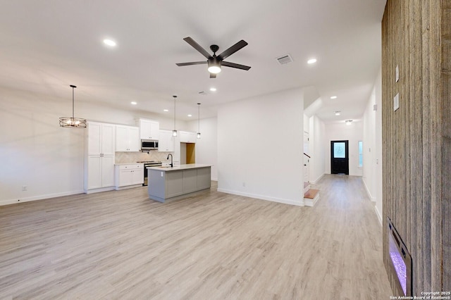 unfurnished living room featuring ceiling fan with notable chandelier, light wood-type flooring, and sink