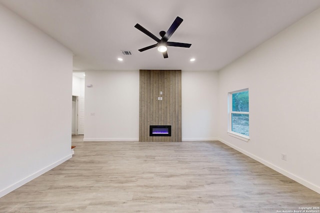 unfurnished living room with ceiling fan, a large fireplace, and light wood-type flooring