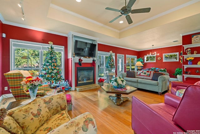 living room with a raised ceiling, a large fireplace, light hardwood / wood-style flooring, and ceiling fan with notable chandelier