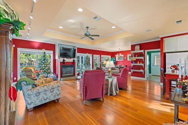 living room with ceiling fan with notable chandelier, light hardwood / wood-style floors, a tray ceiling, and track lighting