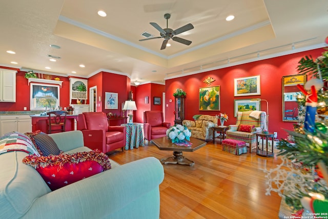 living room with track lighting, light hardwood / wood-style flooring, ceiling fan, and a tray ceiling