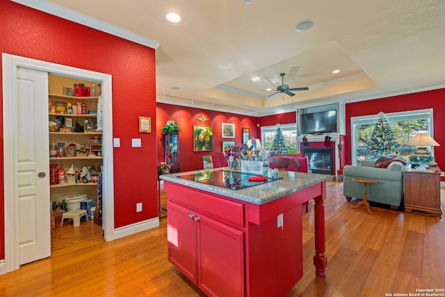 kitchen featuring black electric stovetop, built in shelves, a raised ceiling, light hardwood / wood-style flooring, and a kitchen island