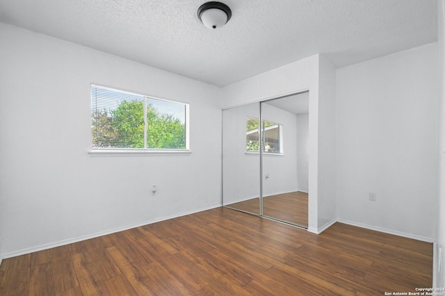 unfurnished bedroom featuring a textured ceiling, dark hardwood / wood-style flooring, and a closet