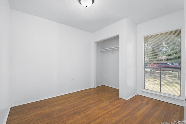 unfurnished bedroom featuring a textured ceiling, multiple windows, a closet, and dark hardwood / wood-style floors