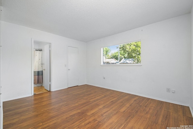 unfurnished bedroom with dark hardwood / wood-style floors, a textured ceiling, connected bathroom, and a closet