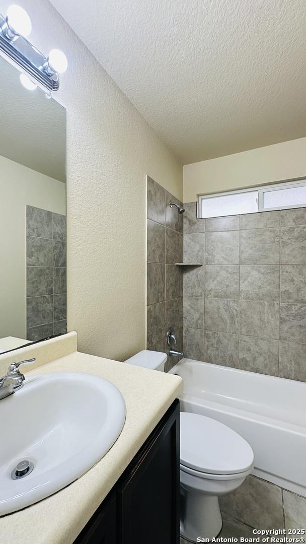 full bathroom featuring vanity, tile patterned floors, tiled shower / bath, toilet, and a textured ceiling