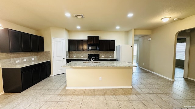 kitchen with decorative backsplash, a center island with sink, light tile patterned floors, and white refrigerator