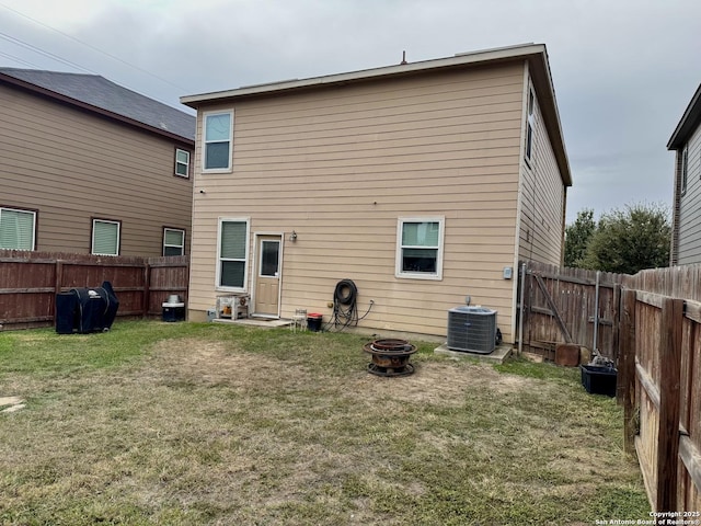 back of house with central air condition unit, a yard, and an outdoor fire pit