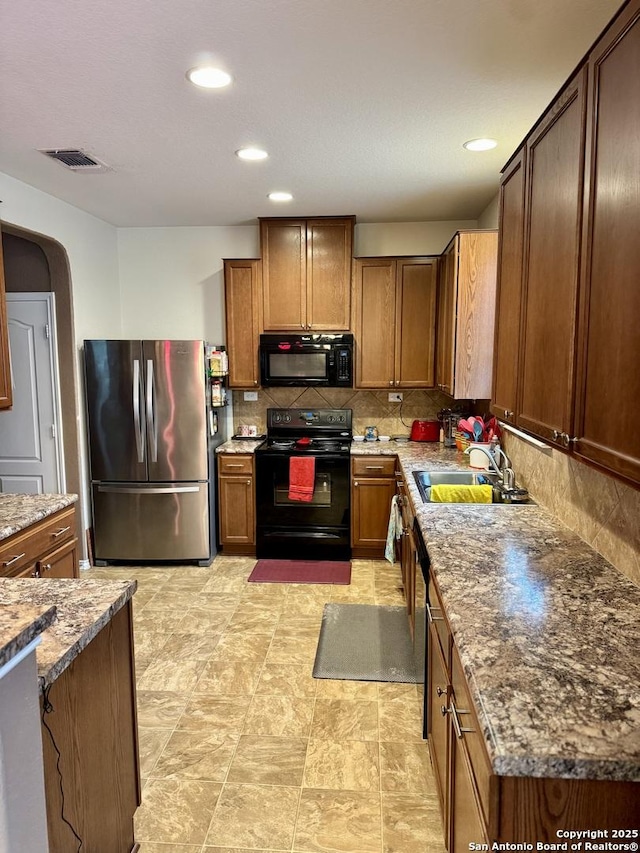 kitchen with sink, tasteful backsplash, dark stone countertops, and black appliances