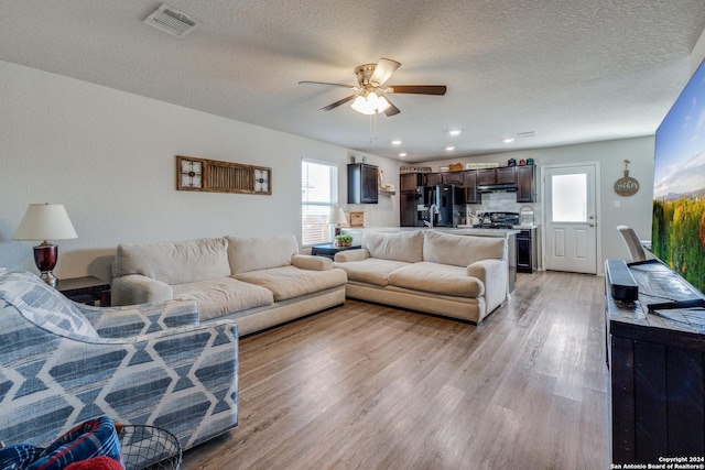 living room with ceiling fan, a textured ceiling, and light hardwood / wood-style flooring