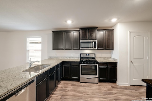 kitchen featuring light stone countertops, sink, stainless steel appliances, kitchen peninsula, and light hardwood / wood-style floors