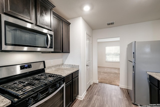 kitchen with light stone countertops, dark brown cabinets, light wood-type flooring, and appliances with stainless steel finishes