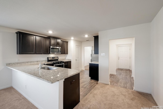 kitchen with dark brown cabinetry, sink, stainless steel appliances, light stone counters, and kitchen peninsula