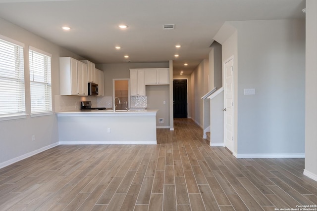 kitchen with backsplash, kitchen peninsula, light hardwood / wood-style flooring, and white cabinets