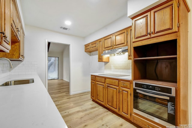 kitchen with decorative backsplash, light wood-type flooring, black electric cooktop, sink, and oven