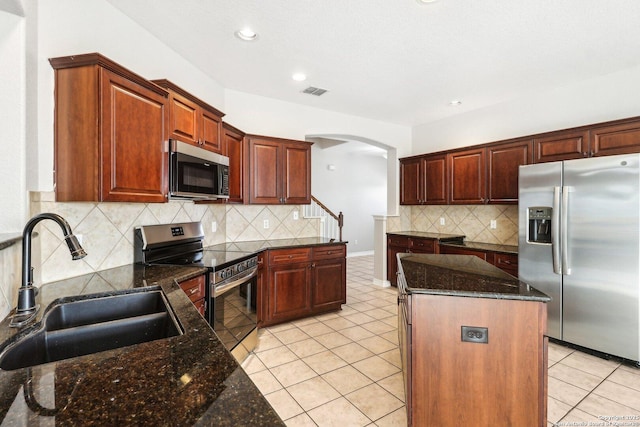 kitchen featuring a center island, sink, dark stone countertops, light tile patterned floors, and stainless steel appliances