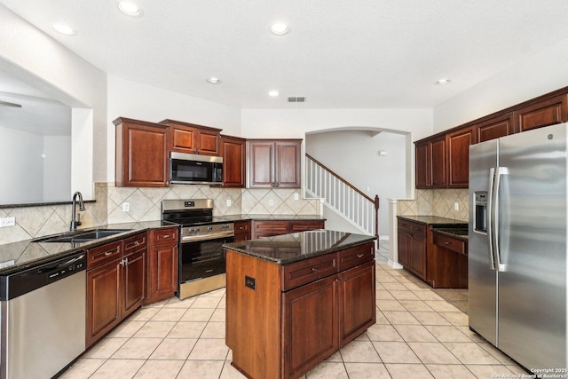 kitchen with stainless steel appliances, sink, light tile patterned floors, dark stone countertops, and a center island