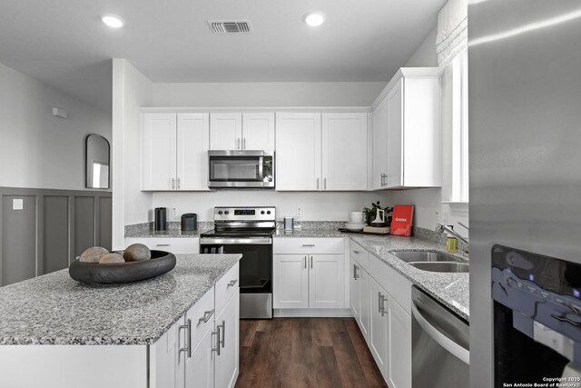 kitchen with dark wood-type flooring, white cabinets, sink, light stone counters, and stainless steel appliances