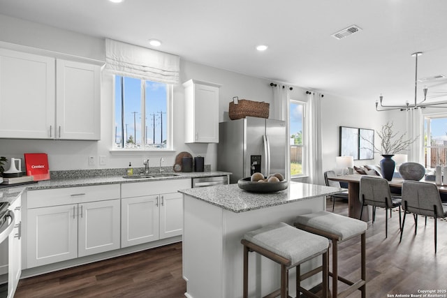 kitchen with appliances with stainless steel finishes, sink, white cabinets, a center island, and a chandelier