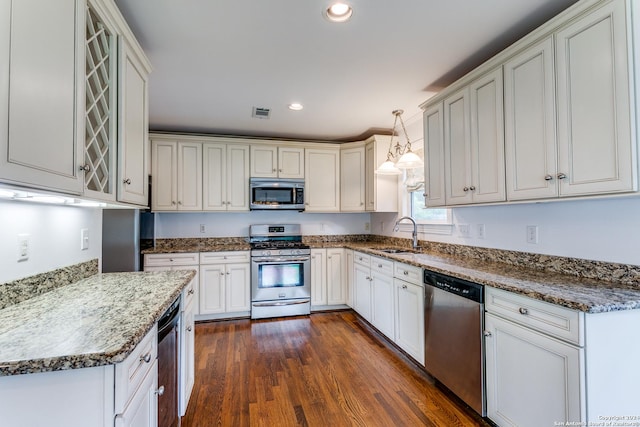 kitchen featuring sink, stainless steel appliances, dark hardwood / wood-style floors, dark stone counters, and decorative light fixtures