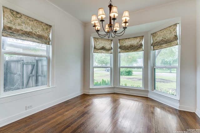 unfurnished dining area with plenty of natural light, dark hardwood / wood-style flooring, crown molding, and an inviting chandelier