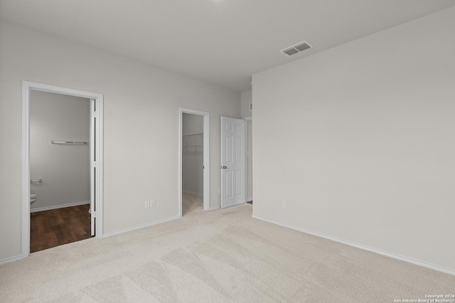 unfurnished bedroom featuring a walk in closet, ensuite bathroom, a closet, and light colored carpet