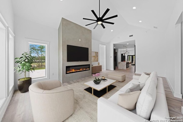 living room with ceiling fan, a fireplace, high vaulted ceiling, and light wood-type flooring