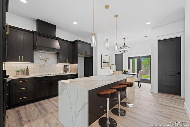 kitchen featuring decorative backsplash, a kitchen breakfast bar, wall chimney range hood, decorative light fixtures, and an island with sink