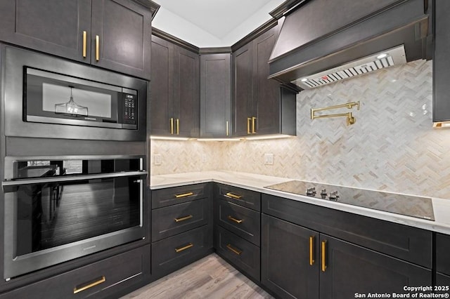 kitchen featuring premium range hood, light hardwood / wood-style flooring, decorative backsplash, appliances with stainless steel finishes, and dark brown cabinets