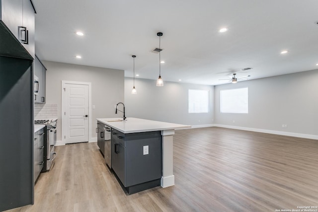 kitchen with ceiling fan, stainless steel appliances, light hardwood / wood-style floors, decorative light fixtures, and a kitchen island with sink