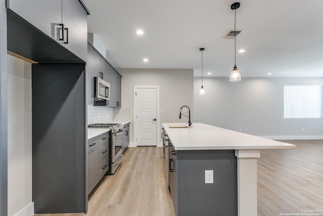 kitchen with tasteful backsplash, stainless steel appliances, sink, pendant lighting, and light hardwood / wood-style flooring